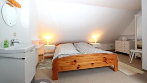 A bedroom with a wooden bed, two bedside tables with lamps, a white dresser, a round mirror, and a white sink. - Lorenz (Hörnum (Sylt))