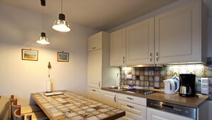 A kitchen with white cabinets, a wooden countertop, a sink, a coffee maker, and a table with a placemat. - Lorenz (Hörnum (Sylt))