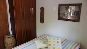 A bedroom with a bed, striped bedding, a wooden wardrobe, a wicker basket, and a framed picture on the wall.
