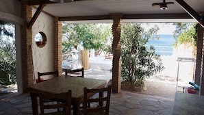 An outdoor patio with a table and chairs, a hanging light fixture, and a view of the beach and ocean.