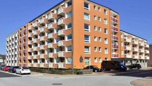 A multi-story residential building with balconies, a parking area, and a clear sky. - Windhuk, Brandenburger Str. 6, Wohnung 51, 4 Etage (Sylt)