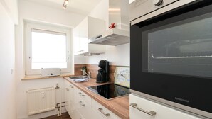 A modern kitchen with white cabinets, a black oven, and a window above the sink. - Wohnung Lee (Sylt)