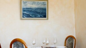 A dining table set with plates, glasses, and cutlery, with a framed painting of a stormy sea above it. - Wohnung Lee (Sylt)