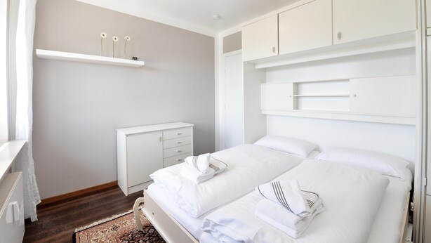 A modern hotel room with a large bed, a bedside table, a wardrobe, and a small shelf with decorative items. - Wohnung Lee (Sylt)