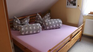 A single bed with a wooden frame, a pink mattress, and heart-patterned pillows. - Ferienwohnung Däumler (Breitenbrunn/Erzgeb.)
