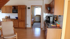 A kitchen with wooden cabinets, a microwave, and a sink. There is a chair and a red rug in the foreground. - Ferienwohnung Däumler (Breitenbrunn/Erzgeb.)