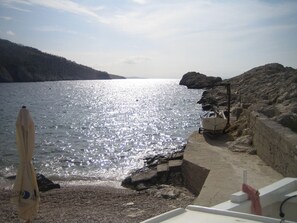 A boat docked at a rocky shore with a clear view of the water and distant hills. - Casa Poseidon (Jelsa)