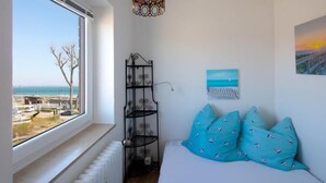 A bedroom with a view of the sea, a radiator, a metal shelf, and a bed with patterned pillows. - Seetempel 34 Scharbeutz (Scharbeutz)