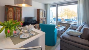 A modern living room with a sofa, a teal armchair, a dining table with a white tablecloth, and a television. - Seetempel 34 Scharbeutz (Scharbeutz)