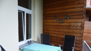 A small outdoor patio with a table covered by a checkered tablecloth, two chairs, a window, and a decorative wall piece. - Vis-a-vis Berliner Tor (Schwerin)