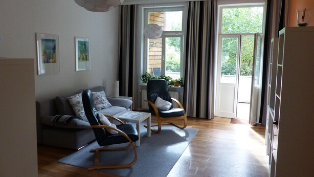 A living room with a sofa, two rocking chairs, a coffee table, and a large window with curtains. - Vis-a-vis Berliner Tor (Schwerin)