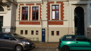 A building with multiple windows and a door, a parking area with two cars, and a street lamp. - Vis-a-vis Berliner Tor (Schwerin)