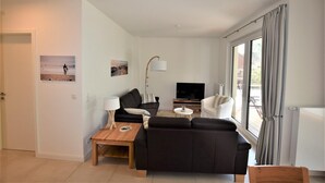 Un salon moderne avec un canapé, une table basse, un téléviseur et une grande fenêtre avec des rideaux.