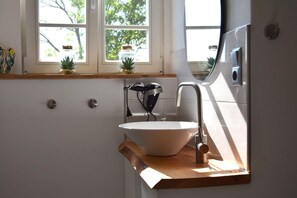 A modern kitchen with a white sink, stainless steel faucet, and a wooden countertop. There are two potted plants on the windowsill and a hairdryer on the counter.