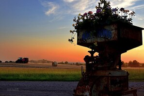 A rural landscape with a vintage water pump in the foreground, set against a sunset sky.