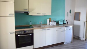 Une cuisine compacte avec des meubles blancs, un four encastré, un lave-vaisselle et un pare-feu de couleur turquoise.