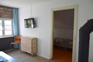 A room with a wooden dresser, a chair, a television mounted on the wall, and a bed with a blanket.