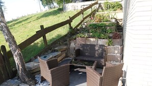 An outdoor patio with wicker furniture, a stone pathway, and a small garden area with plants. - Haus Panoramablick (Sundern)