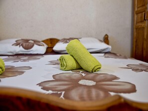 Un lit avec une couvre-lit à motifs floraux, deux serviettes enroulées et une tête de lit en bois.