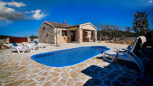 A stone house with a swimming pool and lounge chairs.
