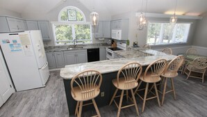 A kitchen with a central island, wooden chairs, a refrigerator, and a window with blinds. - Soundfront, Sound View, Hot Tub, Community Amenities, 528, Celestial Haven (Corolla)