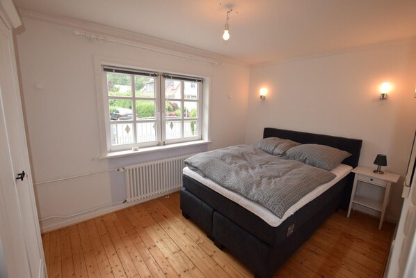 A bedroom with a bed, a window, a radiator, and a nightstand. - Haus am Strandweg H $$$$$ (Hohwacht)