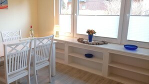 A dining area with a table and chairs, a vase with flowers, and a window with blinds.