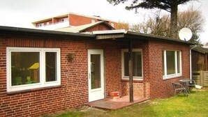 A single-story brick house with a front door, two windows, a satellite dish, and a small patio area.