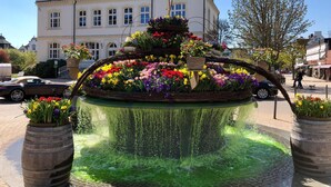 A fountain with a tiered flower arrangement in front of a building with multiple windows and a balcony. - Schoenhier-timmendorf (Timmendorfer Strand)