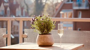 A potted plant with flowers on a balcony table, a glass of white wine, and a railing. - Schoenhier-timmendorf (Timmendorfer Strand)