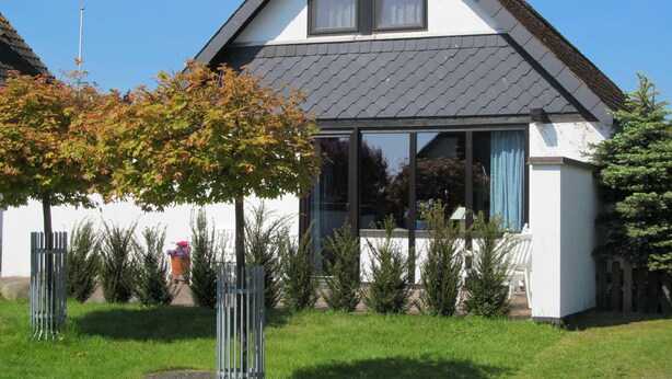 Una casa de dos pisos con fachada blanca, techo oscuro y ventanas amplias.