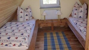A small, cozy attic bedroom with two single beds, a window, and a wooden bench. - Zur Alten Schmiede II Wohnung Oben I (Boltenhagen)