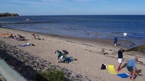 A beach with people sunbathing and swimming, a rocky shoreline, and a clear sky. - Zur Alten Schmiede II Wohnung Oben I (Boltenhagen)