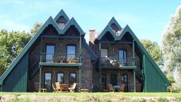 A two-story lodge with a steeply pitched roof, wooden balcony railings, and a stone facade. - Zur Alten Schmiede II Wohnung Oben I (Boltenhagen)