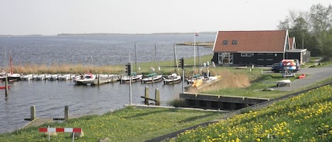 Uma marina com barcos atracados, um pequeno edifício com telhado vermelho e uma área gramada com flores amarelas.