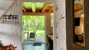 A hallway with a wooden ceiling, a door leading to an outdoor patio with a table and chairs, and a wall-mounted light fixture. - Holiday Home de Druif 6p With a Nice Terrace Near Lake Lauwersmeer (Anjum)
