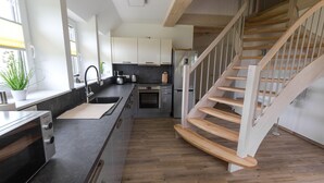 A modern kitchen with a wooden staircase, built-in appliances, and a large window. - Fewo Hiddenseeblick (Dranske)