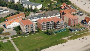 Vista aérea de una zona residencial costera con edificios de varios pisos, una playa de arena y un campo cubierto de césped.