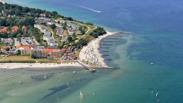Vista aérea de un pueblo costero con playa, puerto deportivo y edificios residenciales.