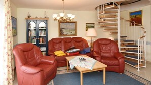 Un salon avec des fauteuils en cuir, une table basse en bois, une bibliothèque et un escalier en colimaçon.