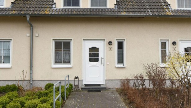 Un immeuble résidentiel de deux étages, doté d’une façade beige, d’un toit recouvert de tuiles et d’une porte blanche située au centre.
