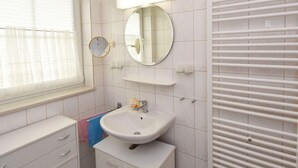 Une salle de bain avec un lavabo, un miroir et une fenêtre équipée de stores.