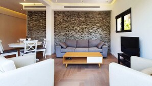 A modern living room with a stone accent wall, a grey sofa, white armchairs, a wooden coffee table, and a flat-screen TV.