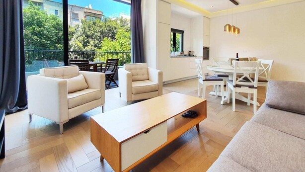 A modern living room with a sofa, two armchairs, a coffee table, and a dining area with a table and chairs.