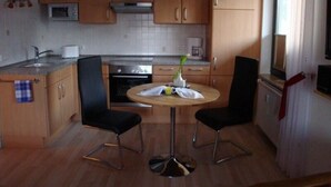 A compact kitchen with wooden cabinets, a microwave, a stove, and a dining table with two chairs. - Apartment Pahl (Langelsheim)