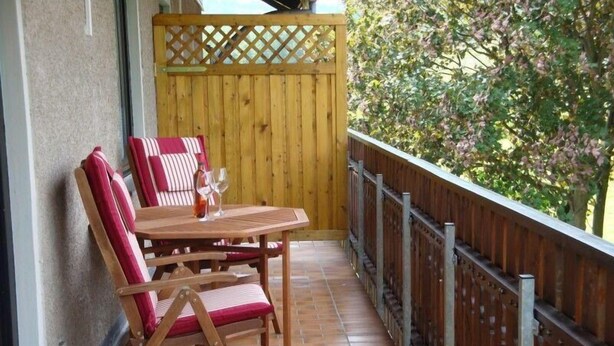 A wooden balcony with a table and chairs, a wooden fence, and a view of greenery. - Apartment Pahl (Langelsheim)
