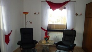 A room with two black leather chairs, a small table with a vase of flowers, a radiator, and a window with curtains. - Apartment Pahl (Langelsheim)