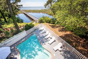 A swimming pool with a deck, lounge chairs, and a wooden bridge over water.