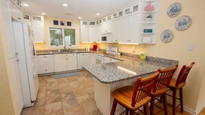 A kitchen with white cabinets, granite countertops, and a central island with bar stools. - Soundfront, Sound views, Private Pool, Hot Tub, MS12, Sounds Amazing (Corolla)