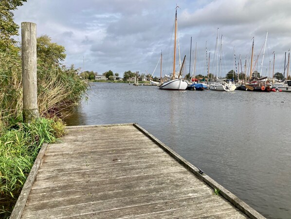 A wooden dock leading to a calm water body with several sailboats docked.